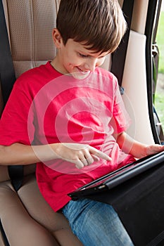 Boy is sitting in a car and playing with ipad.
