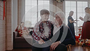 Boy sitting on a chair with his grandad and talking at Christmas celebration