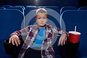 Boy sitting in cinema theatre, watching movie attentively.