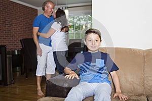 Boy sitting in couch at home, parents in background