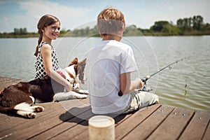 Boy sitting on dock by the river, fishing with his dog and little girl