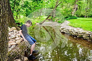 Boy Sitting at edge of stream getting shoes wet