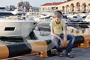 A boy is sitting on an embankment of a resort city, he is upset because all theatres and museums are closed or let