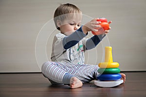 A boy sitting on the floor collects a children`s pyramid.