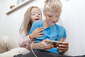 boy is sitting on the floor and playing mobile games on her phone. girl sits next to him and worries about the process of playing