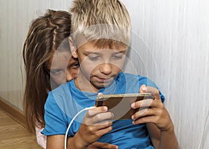 boy is sitting on the floor and playing mobile games on her phone. girl sits next to him and worries about the process of playing