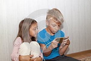 boy is sitting on floor and playing mobile games on his phone. girl sits next to him and worries about the process of playing a