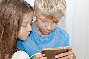 boy is sitting on floor and playing mobile games on his phone. girl sits next to him and worries about the process of playing