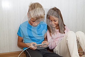 boy is sitting on floor and playing mobile games on his phone. girl sits next to him and worries about the process of playing