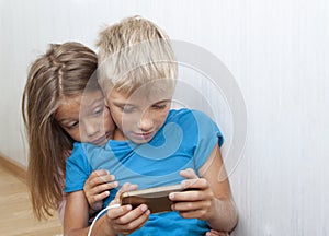 boy is sitting on the floor and playing mobile games on phone. girl sits next to him and worries about the process of playing a