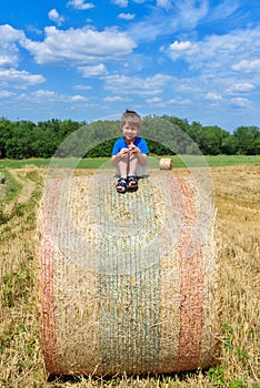 The boy is sitting on golden hay bales on the field