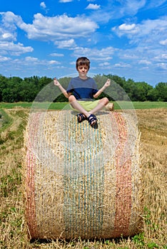 The boy is sitting on golden hay bales on the field