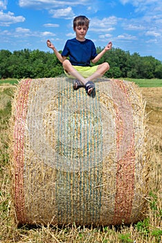 The boy is sitting on golden hay bales on the field