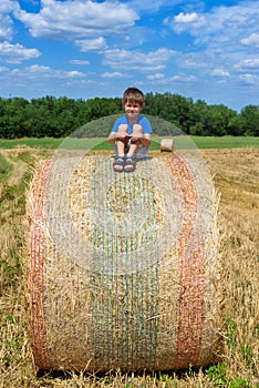 The boy is sitting on golden hay bales on the field