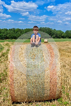 The boy is sitting on golden hay bales on the field