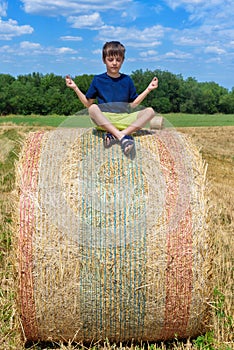 The boy is sitting on golden hay bales on the field