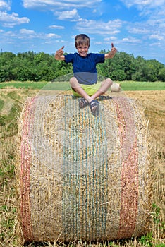 The boy is sitting on golden hay bales on the field