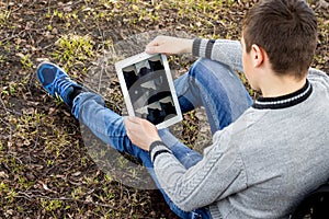 Boy is sitting on grass and looking at tablet. Modern technolo
