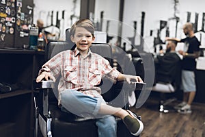 The boy is sitting in the hairdresser`s barber shop.