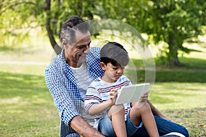 Boy sitting on his fathers lap and using digital tablet in park