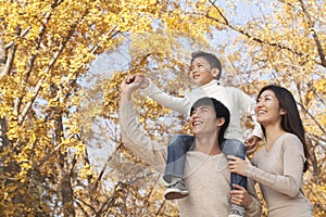 Boy sitting on his fathers shoulders in a park with family in Autumn