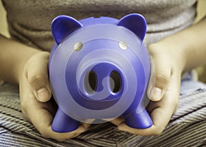 Boy sitting holding a blue piggy bank in hand, concept of financial planning for education, saving and depositing money in the