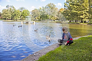 Boy sitting by lake in Boston public garden with geese