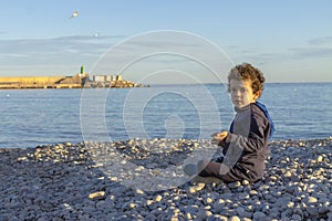 Boy sitting on pebble beach looking at the camera at sunset