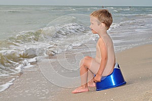 Boy sitting on a potty on the seashore