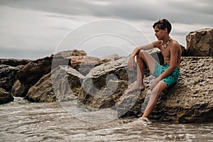 Boy sitting on the rock with leg in the water