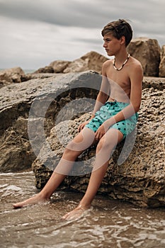 Boy sitting on the rock with legs in the water