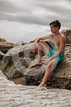 Boy sitting on the rock while waves hitting his leg