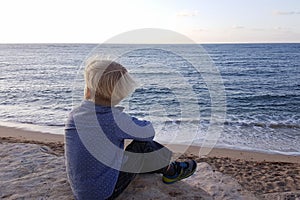 Boy sitting on rocks near sea shore waiting