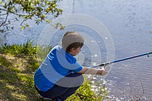 The boy is sitting on the shore of the lake with a fishing rod and fishing. The little fisherman. A child is fishing in the river