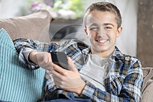 Boy sitting on sofa texting on mobile phone, happy and smiling background