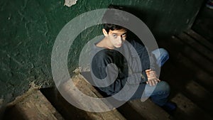 The boy is sitting on the steps of an abandoned porch. The concept of children`s drug addiction, vagrancy, homelessness.