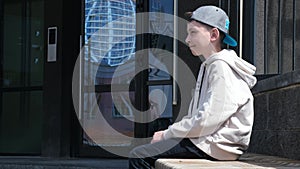 The boy is sitting on the street, dreaming about the future of his life. Thoughtful boy is sitting on a bench. Teenage life.