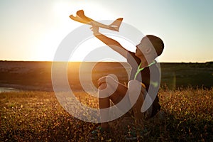 Boy sitting at sunset with an airplane in his hand