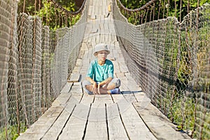 The boy is sitting on the suspension bridge. His eyes are closed. He is resting. (concept of balance)