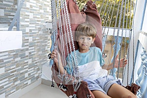 Boy is sitting, swinging in rattan swing chair during summer holidays , outdoors having fun.