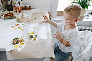 boy sitting at the table drawing with paints