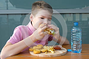 Boy sitting at a table eating fast food and drinking water, close-up