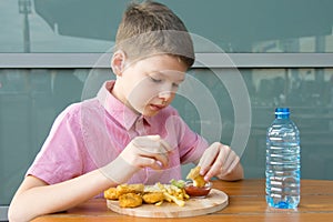 A boy sitting at a table eating fast food, nuggets with sauce