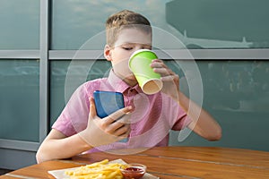 The boy sitting at the table has lunch and looks at the phone, decides his future plans