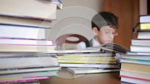 Boy sitting at a table with a stack of books. child reading. boy with glasses