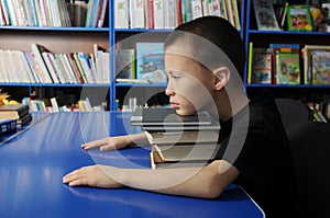 Boy sitting tired on pile of books in library don`t want to learning