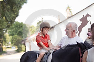 A boy sitting on top of a black horse listening to his grandfather's instruction