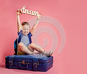 Boy sitting on the travel bag and dreaming. Dream of future. Child with backpack and sleepers want to go on summer