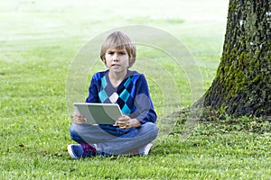 The boy sitting under a big tree with the tablet PC. Technology, lifestyle, education, people concept