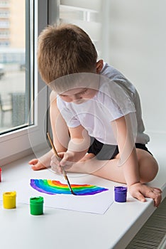 Child at home draws a rainbow on the paper sheet photo